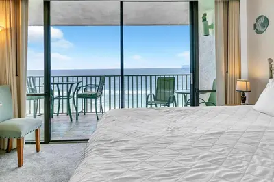 a bedroom with a bed and a balcony with chairs at Windward 604 at Edgewater in Panama City Beach
