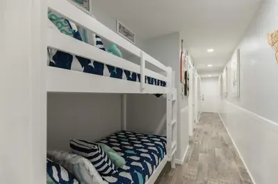 a white room with a bunk bed with a bench at The Summit 504 in Panama City Beach