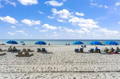 a group of people sitting on a beach with blue umbrellas at The Summit 1017 in Panama City Beach