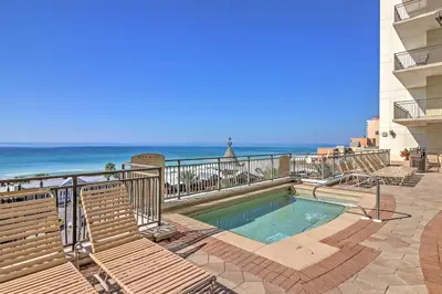 a swimming pool with chairs and the ocean in the background at Chic Panama City Beach Condo with Pool and Gulf Views in Panama City Beach