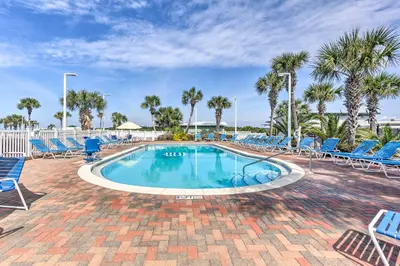 a swimming pool with blue chairs and palm trees at Panama City Beach Retreat with Pool and Ocean Views! in Panama City Beach