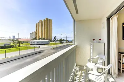 a balcony with two white chairs and a view of a street at PCB Condo with Pool and Grill Access - Walk to Beach! in Panama City Beach