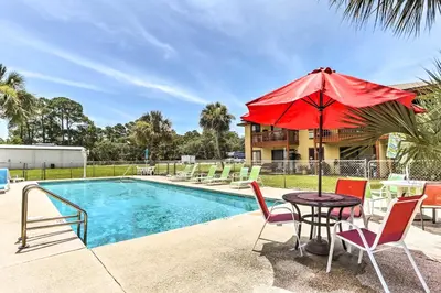 a table with a red umbrella next to a pool at Cute PCB Condo by Lake Powell with Pool Access! in Panama City Beach