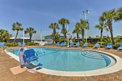 a swimming pool with blue chairs and palm trees at Oceanfront PCB Condo with Beach Access and 2 Pools in Panama City Beach