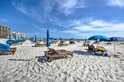 a beach with chairs and umbrellas and people on it at Panama City Beach Condo with Balcony and Ocean Views in Panama City Beach