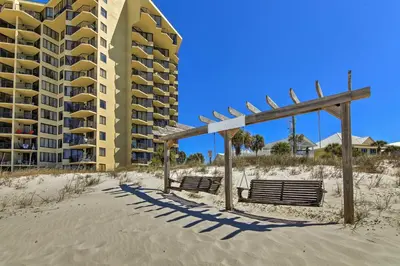 two benches on the beach in front of a building at Bright PCB Condo with Gulf Views and Beach Access! in Panama City Beach