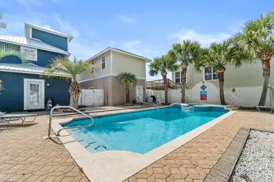 a swimming pool in front of a house with palm trees at Panama City Beach House - Sunnyside Up in Panama City Beach