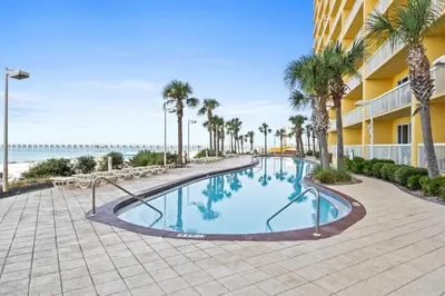 a swimming pool at the beach with palm trees and a building at Calypso Beach Resort Towers in Panama City Beach