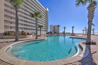 a swimming pool with palm trees in front of a hotel at Comfy PCB Condo with View and Private Beach Access! in Panama City Beach