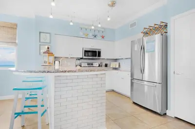 a kitchen with a refrigerator and a counter with a stool at Shores of Panama 1401 in Panama City Beach