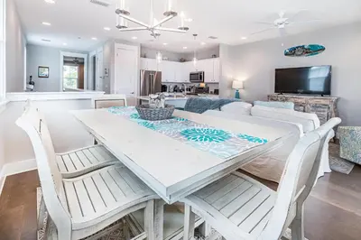 a dining room and living room with a white table and chairs at Inn to the Mystic in Santa Rosa Beach