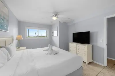 a white bedroom with a white bed and a television at The Summit 606 in Panama City Beach