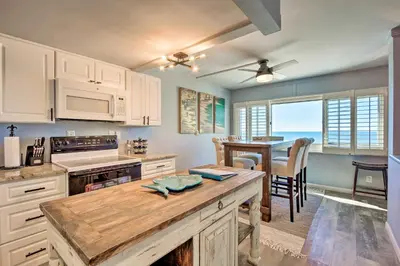 a kitchen with white cabinets and a table and a dining room at PCB Beachfront Coastal Abode at Pinnacle Port! in Panama City Beach