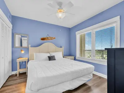 a blue bedroom with a white bed and a window at Grand Panama 2-705 in Panama City Beach
