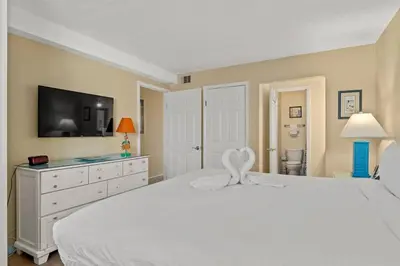 a white bedroom with a white bed and a tv at The Summit 506 in Panama City Beach