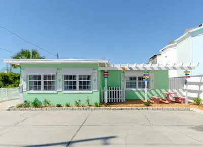 a green and white house with a white fence at Emerald Beach Cottage in Panama City Beach