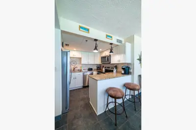 a kitchen with white cabinets and bar stools at Sunbird 1205W 'Compass Rose Penthouse' in Panama City Beach