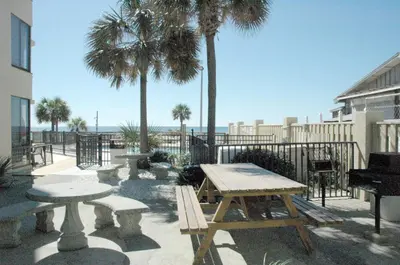 a picnic table and benches with palm trees and the ocean at Sunbird 1205W 'Compass Rose Penthouse' in Panama City Beach