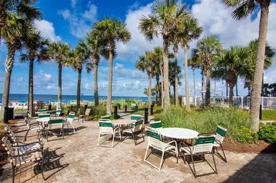 a patio with tables and chairs and palm trees at Grand Panama 1-1803 'Panama Paradise' in Panama City Beach