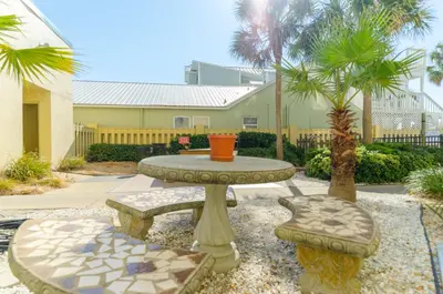 a patio with a table and benches and a palm tree at Sunbird 908E 'High Tides' in Panama City Beach