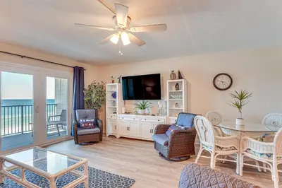 a living room with a table and chairs and a television at Oceanfront PCB Condo Steps to Private Beach! in Panama City Beach