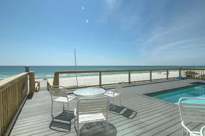 a deck with a table and chairs and the beach at Making Waves - Huge Heated Beachfront Pool & Hot Tub! Best In Pcb! in Panama City Beach