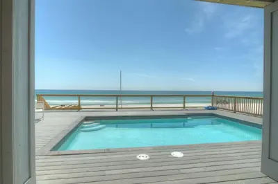 a swimming pool on a deck with a view of the ocean at Making Waves - Huge Heated Beachfront Pool & Hot Tub! Best In Pcb! in Panama City Beach