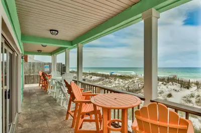 a porch with chairs and tables and a view of the beach at Beachcomber - Beachfront With Pool And Hot Tub - On The Beach! in Panama City Beach