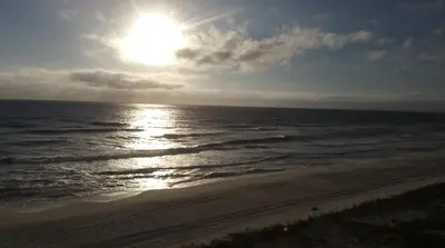 a beach with the sun shining on the water at Tropic Winds Condo in Panama City Beach