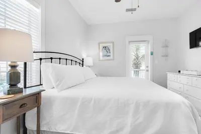 a white bedroom with a bed and a table with a lamp at Seagrove Bungalow 153 in Santa Rosa Beach