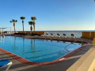 a large swimming pool with chairs and palm trees at Brightly Furnished Beachfront Condo by Brightwild- 7th Floor Gulf View! in Panama City Beach