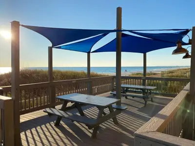 a deck with two picnic tables and a blue umbrella at Brightly Furnished Beachfront Condo by Brightwild- 7th Floor Gulf View! in Panama City Beach