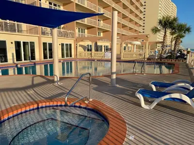 a swimming pool with two chairs and a building at Brightly Furnished Beachfront Condo by Brightwild- 7th Floor Gulf View! in Panama City Beach