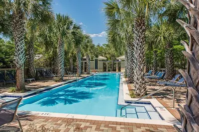 a large swimming pool with palm trees and chairs at Calm Breeze Cottage in Santa Rosa Beach