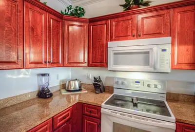 a kitchen with wooden cabinets and a stove and microwave at Fantastic Private Complex -Beachfront 2BD Ocean Villa! Gorgeous Amenities in Panama City Beach