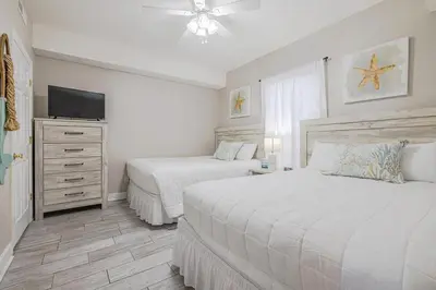 a white bedroom with two beds and a television at Ocean Villa 1102 in Panama City Beach