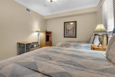 a bedroom with two beds and a desk and a table at Hidden Dunes 1703 in Panama City Beach