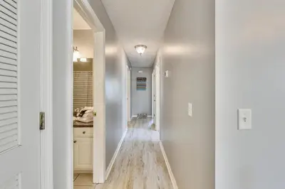 a hallway with white walls and a long hallway with wood floors at Poolside Cabana by Book That Condo in Panama City Beach
