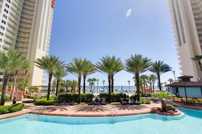 a pool at the resort with palm trees and the ocean at Shores of Panama #2201 by Book That Condo in Panama City Beach