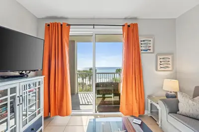 a living room with orange curtains and a view of the ocean at Grand Panama Beach Resort #406-1 by Book That Condo in Panama City Beach
