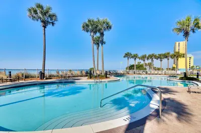 a large swimming pool with palm trees and the ocean at Grand Panama Beach Resort #1707-1 by Book That Condo in Panama City Beach