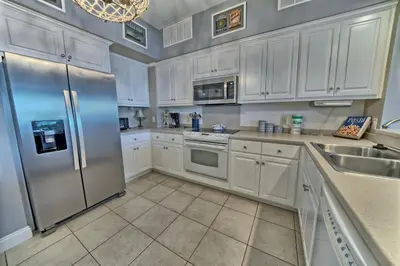 a kitchen with white cabinets and a stainless steel refrigerator at Cozy Oceanfront Condo with Beachside Pool - Unit 1602 in Panama City Beach