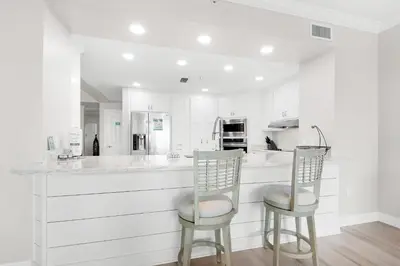 a kitchen with white cabinets and two bar stools at Hidden Dunes 304 in Panama City Beach