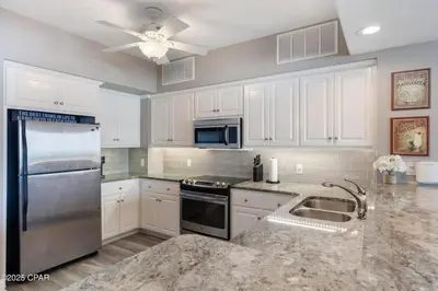 a kitchen with white cabinets and a stainless steel refrigerator at Astonishing Beacfront Condo with 360 sqft Balcony Facing the Ocean - Unit 0302 in Panama City Beach