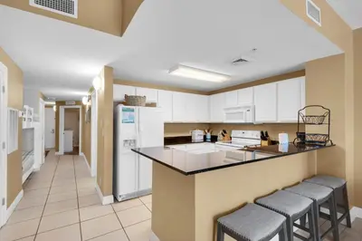 a kitchen with white cabinets and a counter with bar stools at Calypso 1-203 East in Panama City Beach