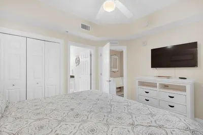 a white bedroom with a bed and a flat screen tv at Calypso 1-203 East in Panama City Beach