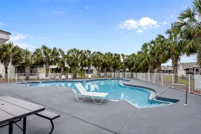 a swimming pool with a table and a bench and palm trees at The Sandbox by Book That Condo in Panama City Beach