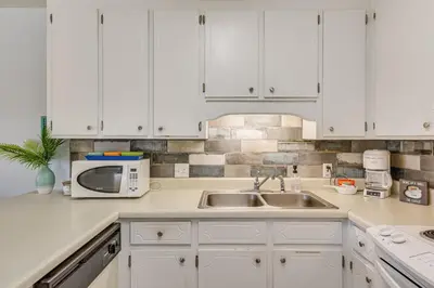 a kitchen with white cabinets and a sink and a microwave at PCB Resort Condo with Private Balcony and 3 Pools! in Panama City Beach