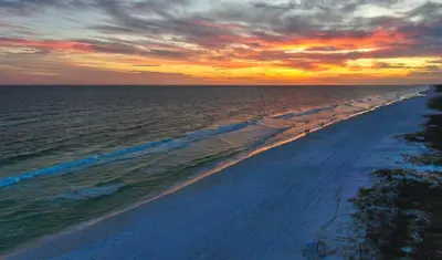 a beach at sunset with people walking on the shore at Ocean Air Upper East Private Beach unit on 30A in Santa Rosa Beach