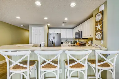 a kitchen with a bar with white stools at Majestic Beach Resort #1303-2 by Book That Condo in Panama City Beach